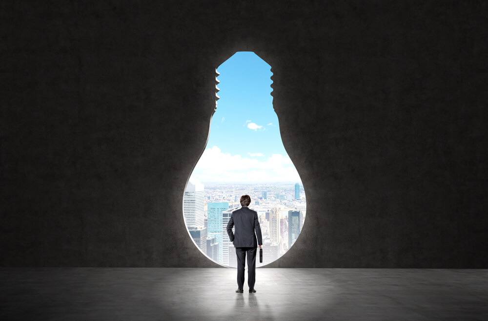 businessman with suitcase standing in front of huge bulb-shaped keyhole