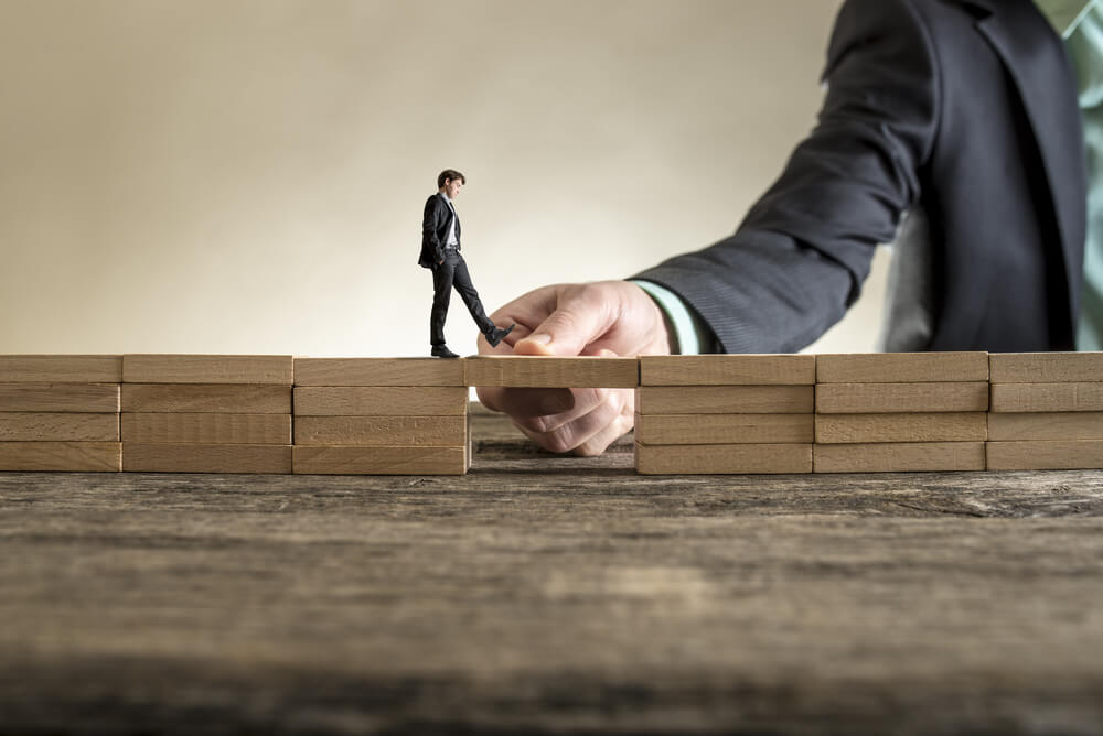 man holding small wooden block as bridge for walking miniature man