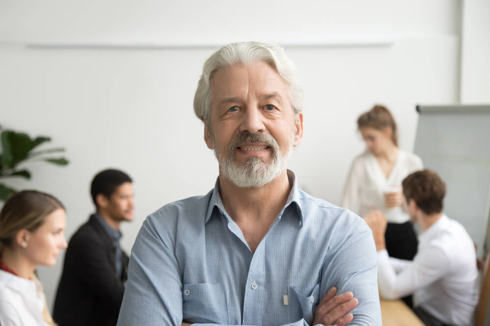male senior executive coach headshot with colleagues in background