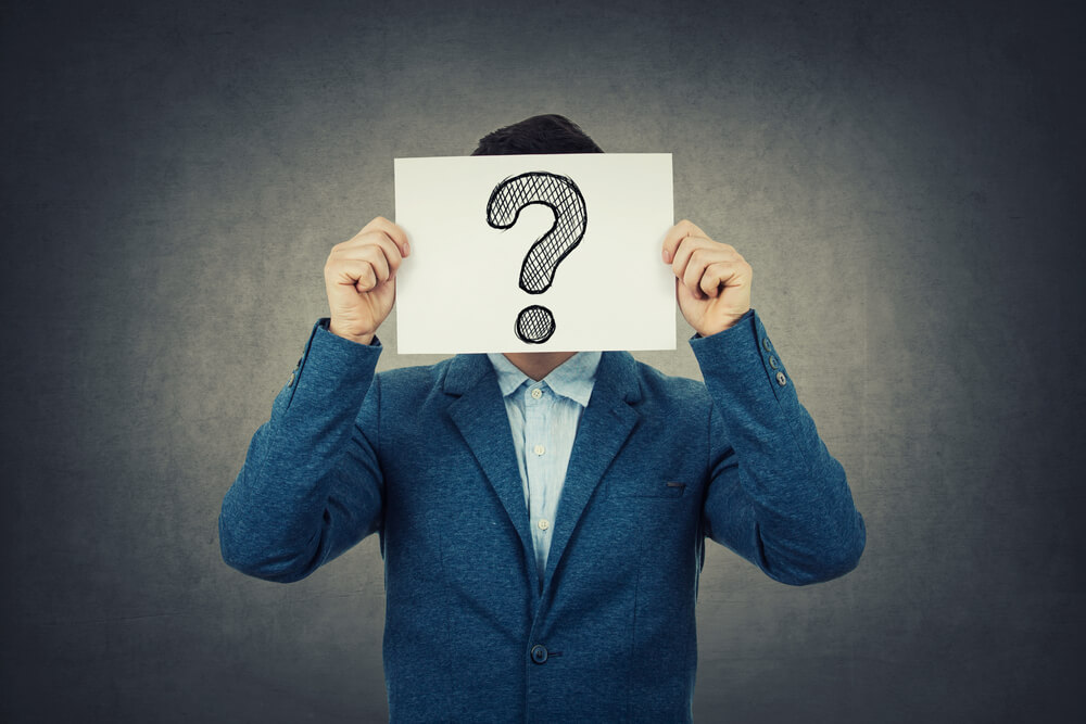 man holding up paper with question mark symbol covering his face