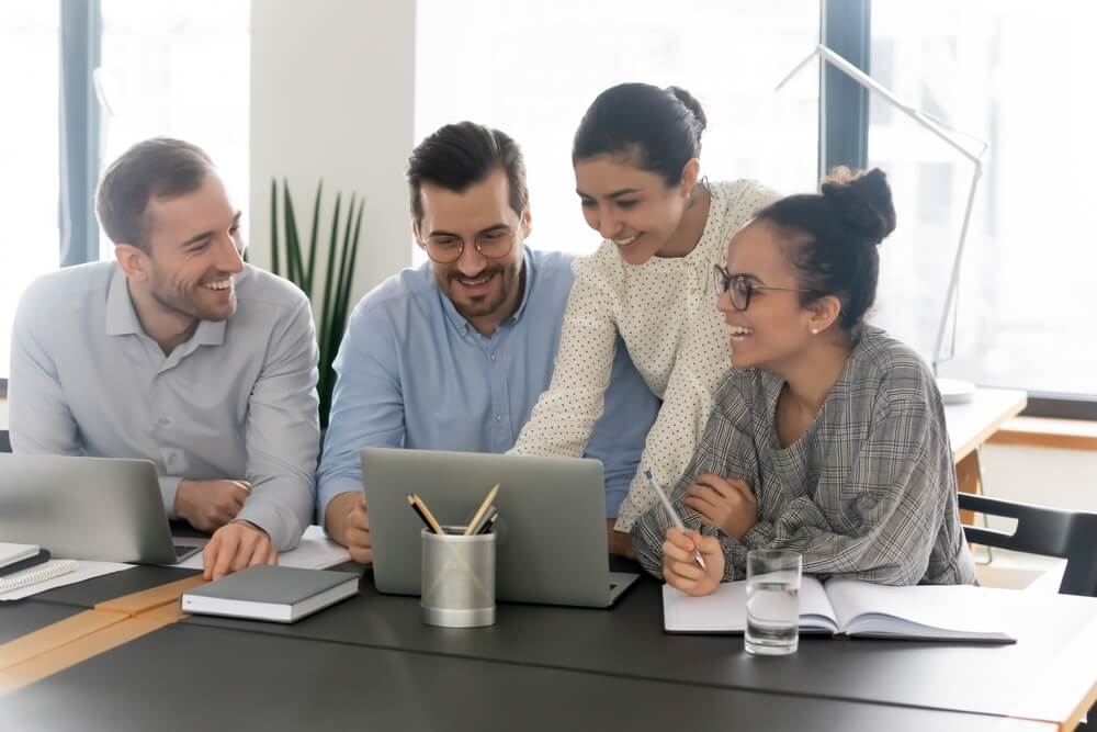 team of diverse employees huddled together on desk with laptop and notes