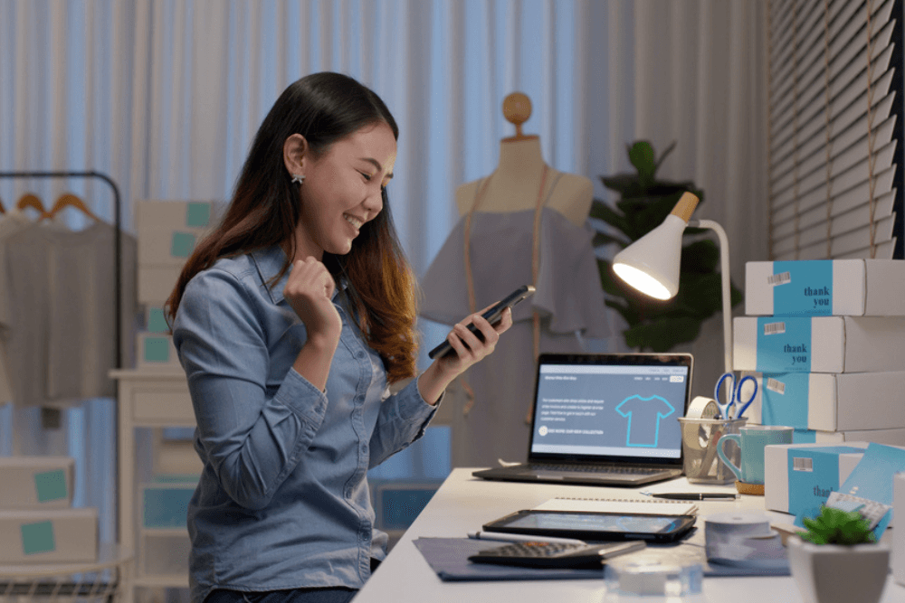 young female entrepreneur in her shop smiling at phone