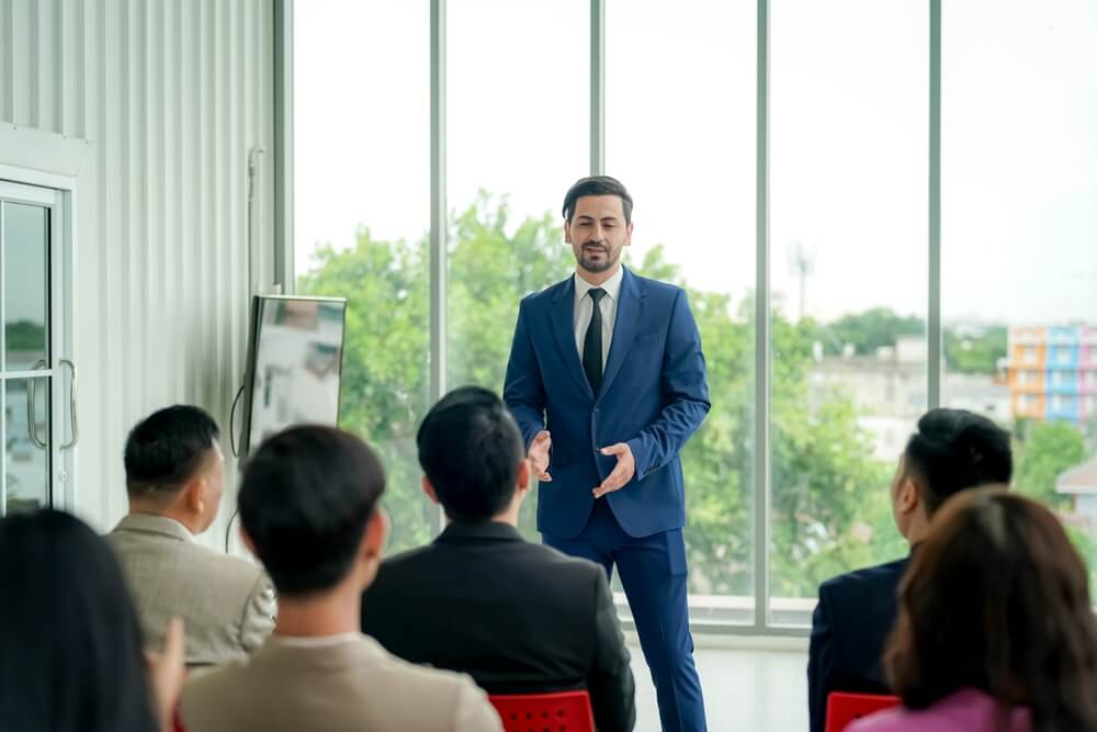 male coach speaking in front of a group of professionals